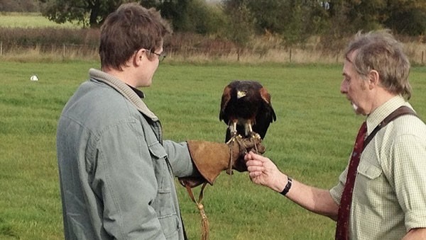 A man holds a bird in his hand and a second man feeds it