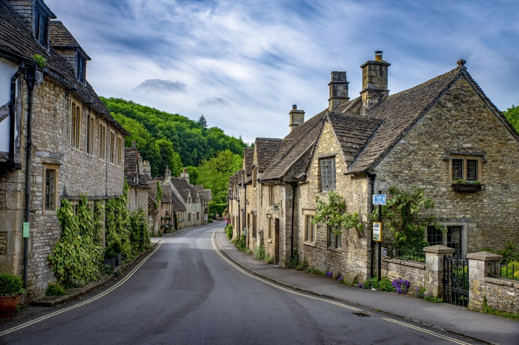 stone houses line a village street with lush greenery and a backdrop of wooded hills