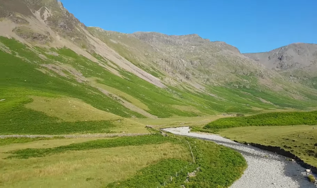 Sunny mountain valley with a winding river and vibrant green meadows